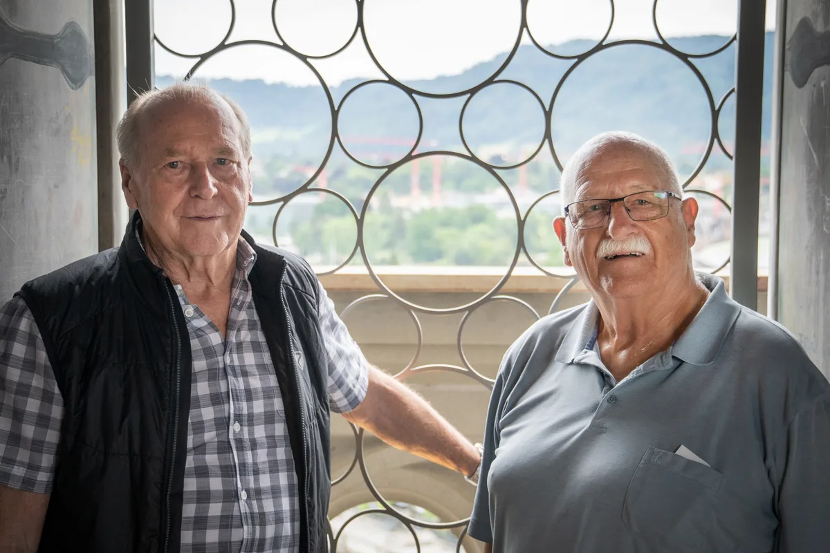 Nach 187 Treppenstufen ist der Ausblick vom 64 Meter hohen Karlsturm in der Altstadt von Zürich wohl verdient. Zwei älteren Herren stehen auf dem Plateau des Karlsturms des Grossmünsters und blicken in die Kamera.